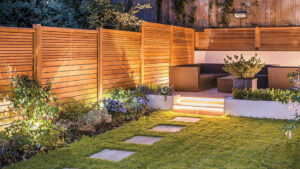 Backyard with wooden privacy fence, garden lights, green lawn, stepping stones, and a patio area with outdoor seating and planters.