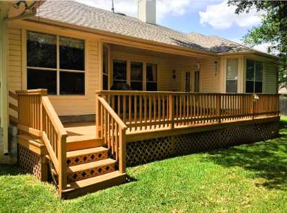 A wooden deck with steps and professional railing installation is attached to the back of a beige house, overlooking a grassy backyard.