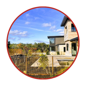 Modern two-story house with large windows and a fenced yard, set against a backdrop of trees and a blue sky with scattered clouds.