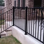 %Imagetitle% | Discount Fence Usa A black metal railing runs along the edge of a raised concrete patio with brick columns, steps, and outdoor furniture.