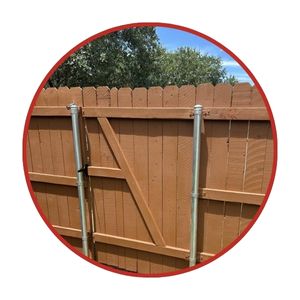 Wooden fence gate reinforced with vertical metal support posts, with trees and blue sky visible in the background.