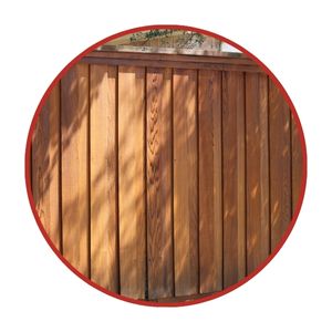 A wooden privacy fence panel with vertical planks, shown within a red circular border. Shadows from nearby foliage fall across the fence.