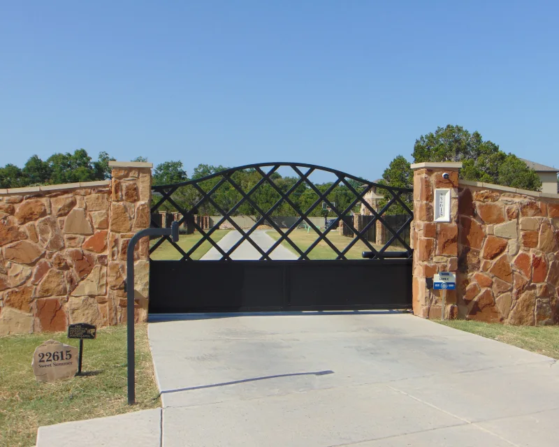 A gated driveway with stone pillars and a black metal gate blocks access to a private property. House number 22615 is displayed on a small sign near the entrance, hinting at recent deck installation work inside.